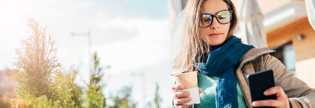 Woman sitting outside wearing glasses on her smartphone